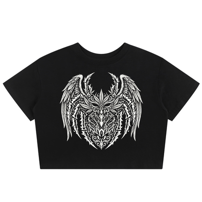A black short-sleeve crop top t-shirt featuring a large white tribal-style graphic of a horned, winged creature on the chest, displayed against a solid white background.