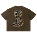 A brown short-sleeve crop top featuring a large, detailed snake graphic on the front. The snake is decorated with a mix of plaid patterns in navy, beige, and brown, outlined with rows of small rhinestones.
