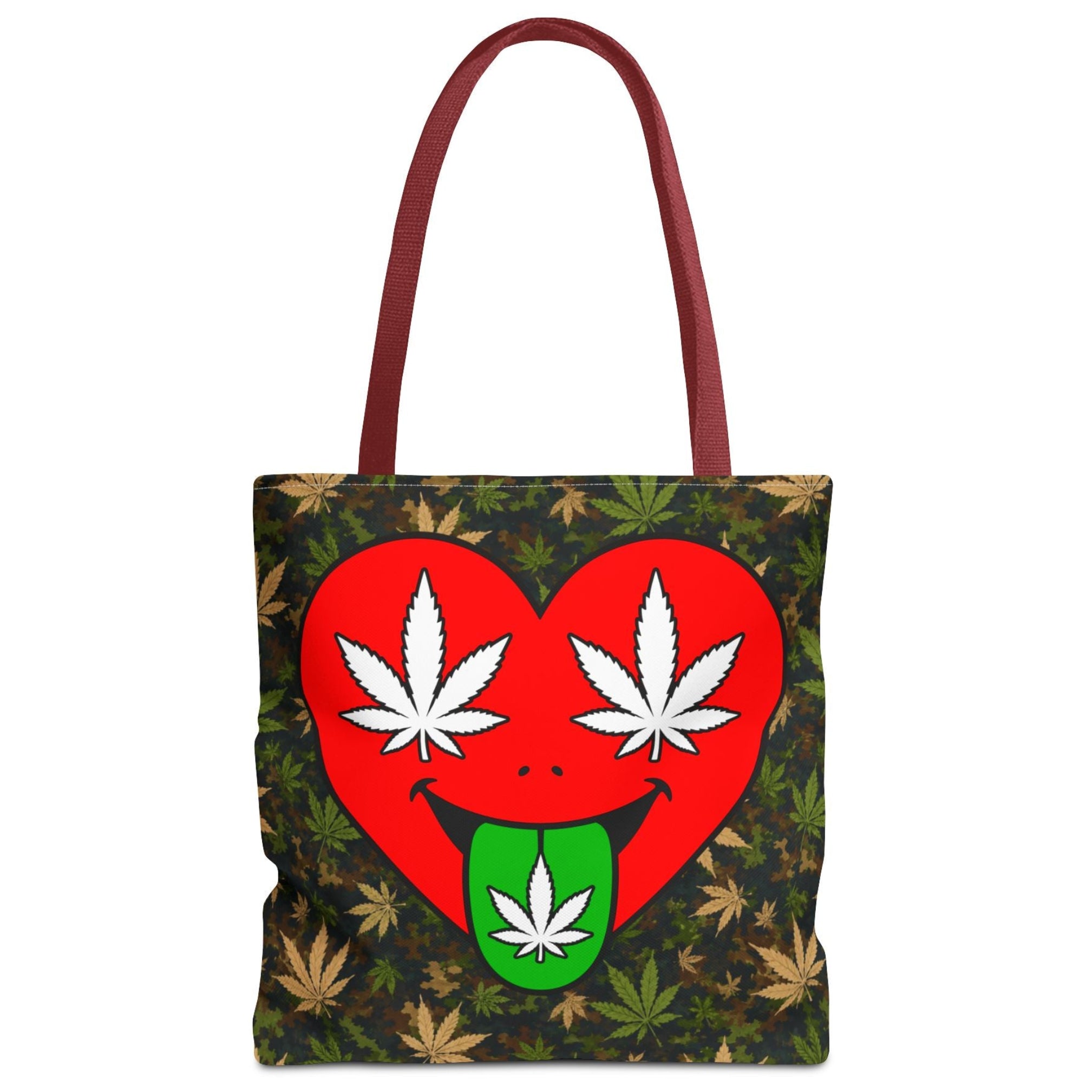 A tote bag with a dark green and brown camouflage leaf pattern, featuring a large red heart graphic on the front with white cannabis leaves for eyes and a green tongue sticking out with a white leaf. The bag has dark red handles.