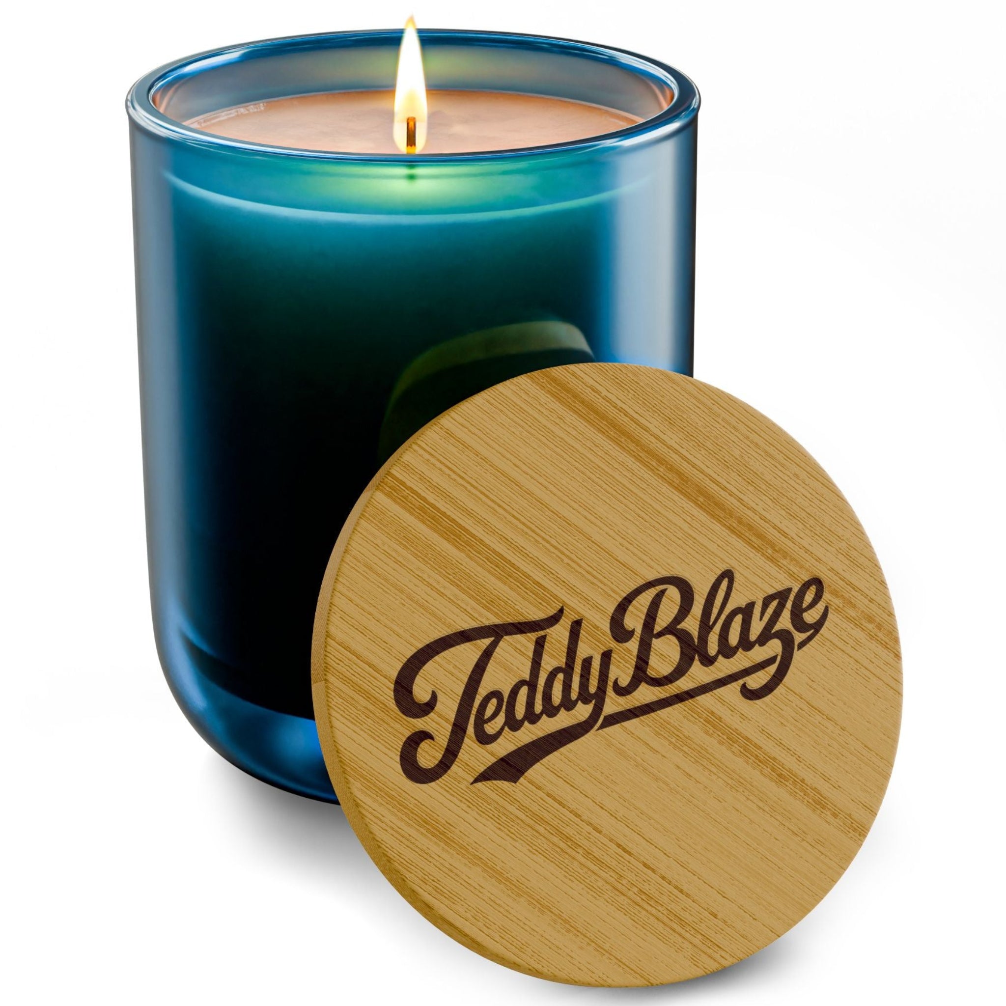 A lit scented candle in a blue-green glass jar with a wooden lid leaning in front, engraved with the brand name 'Teddy Blaze'.