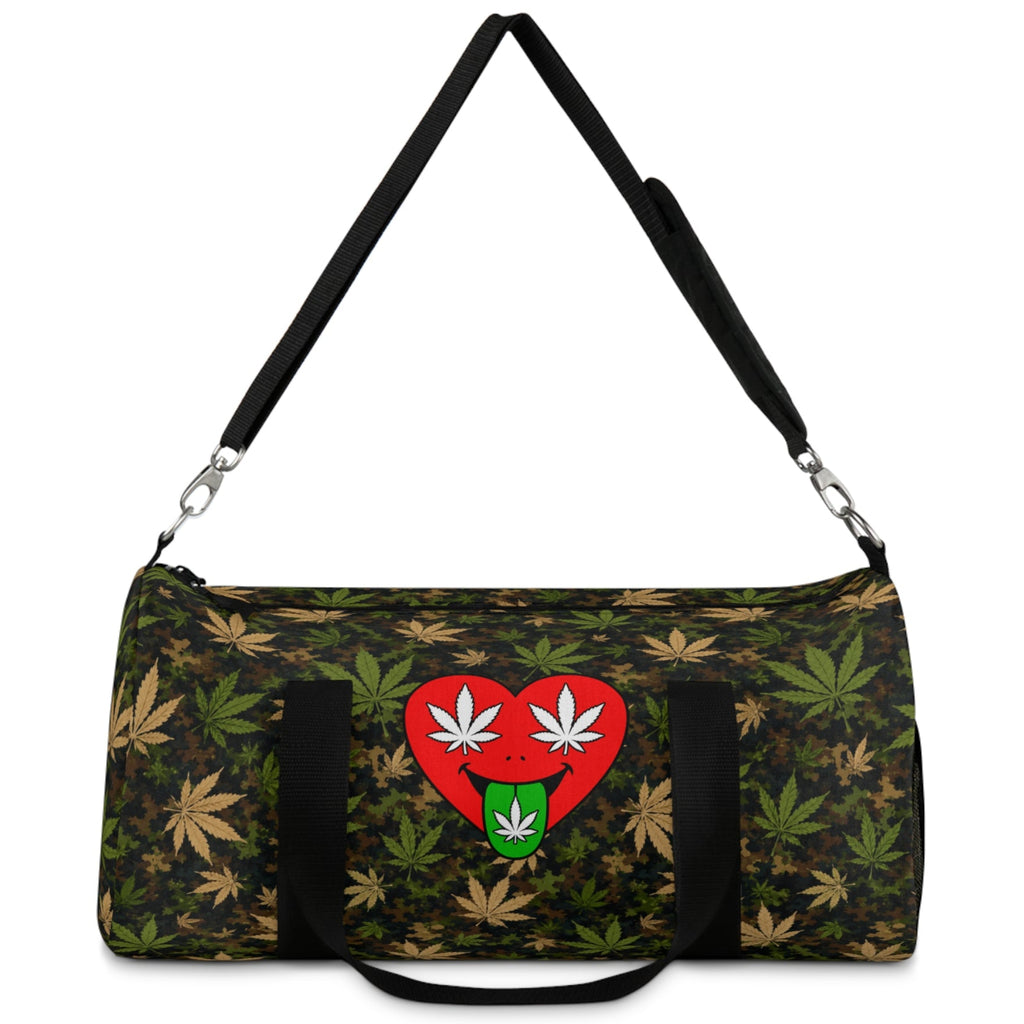 A duffle bag with a dark green and black camouflage pattern overlaid with tan and olive green cannabis leaves. The front features a red heart graphic containing two white cannabis leaves on top and a green marijuana leaf on the bottom.