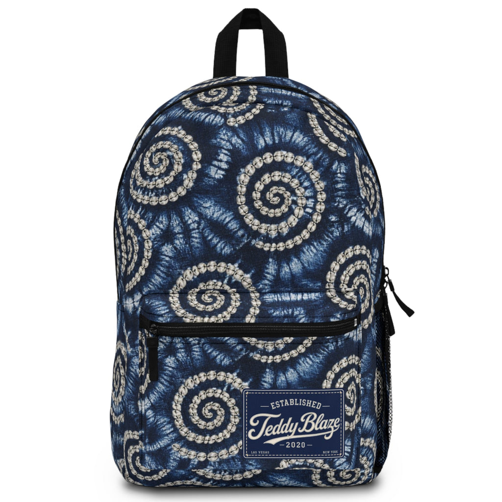 A navy blue backpack with a white spiral tie-dye pattern, featuring a front zippered pocket and a 'Teddy Blaze' brand patch on the front.