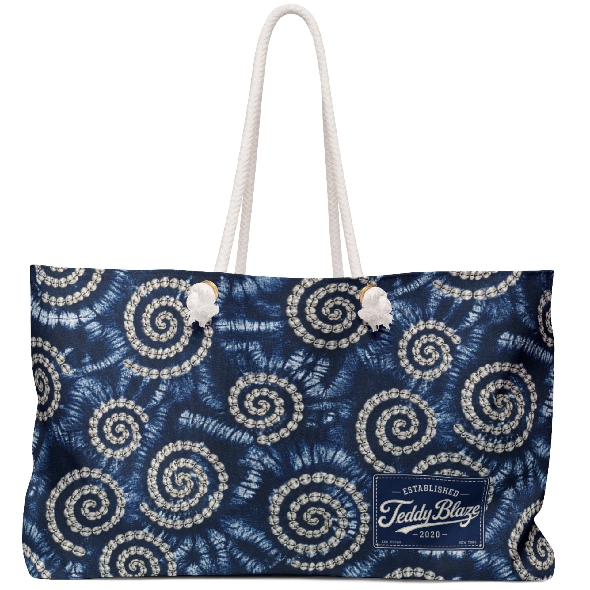 A navy blue tote bag with a white and silver spiral floral pattern, featuring white rope handles and a white embroidered logo on the bottom right.