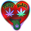 A heart-shaped sticker with a holographic rainbow border, featuring the text 'TEDDY BLAZE' in green and yellow above two cannabis leaves (one purple, one green), with a green tongue sticking out and displaying a purple cannabis leaf.