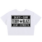 A white short-sleeve crop top t-shirt featuring a black graphic print on the front with the text 'SKATE SURF TEDDY BLAZE LEAF STREETS' and a cannabis leaf icon, displayed on a clean white background.