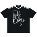 A black short-sleeve t-shirt with white shoulder stripes and a large white 'Teddy Blaze' script logo printed on the front, displayed flat against a solid white background.