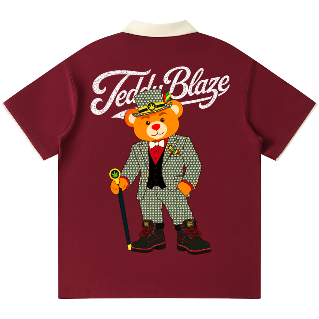 A maroon short-sleeve t-shirt with a cream collar, featuring a large graphic of a teddy bear in a green patterned suit and hat with the text 'Teddy Blaze' printed in white across the upper back.