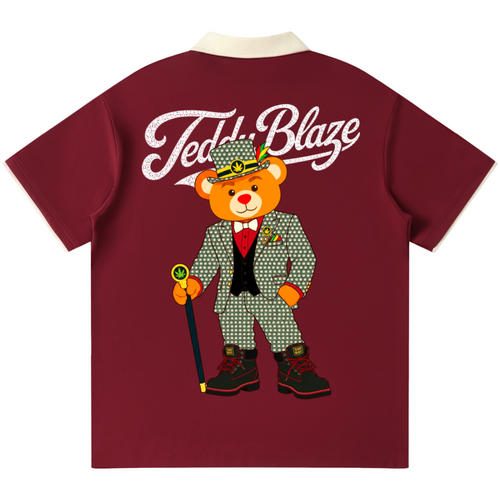 A maroon short-sleeve t-shirt with a cream collar, featuring a large graphic of a teddy bear in a green patterned suit and hat with the text 'Teddy Blaze' printed in white across the upper back.