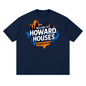 A navy blue short-sleeve t-shirt with a colorful graphic on the chest reading 'WELCOME TO HOWARD HOUSES BROOKLYN NY' over an orange and blue city skyline silhouette.