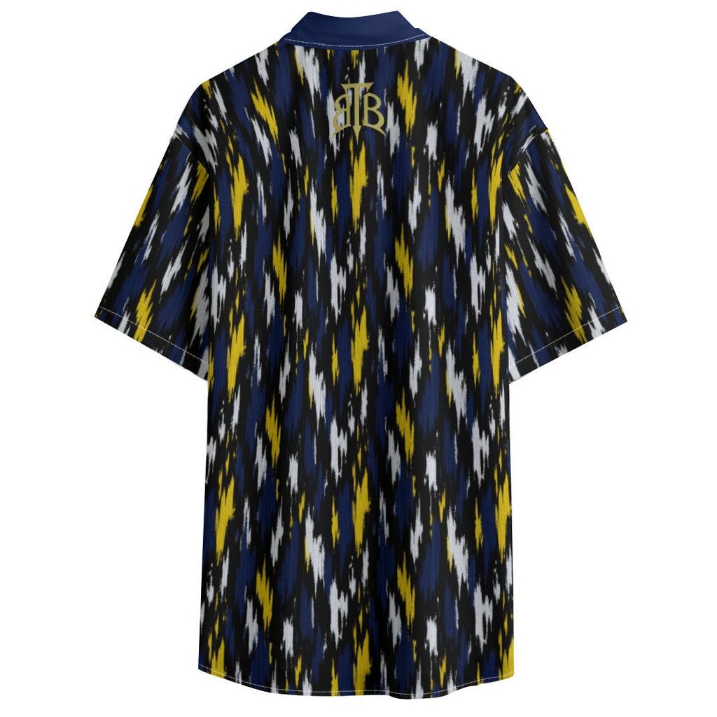 A short-sleeve button-up shirt shown from the back, featuring a navy blue, yellow, and white ikat pattern with a gold monogram logo at the collar.