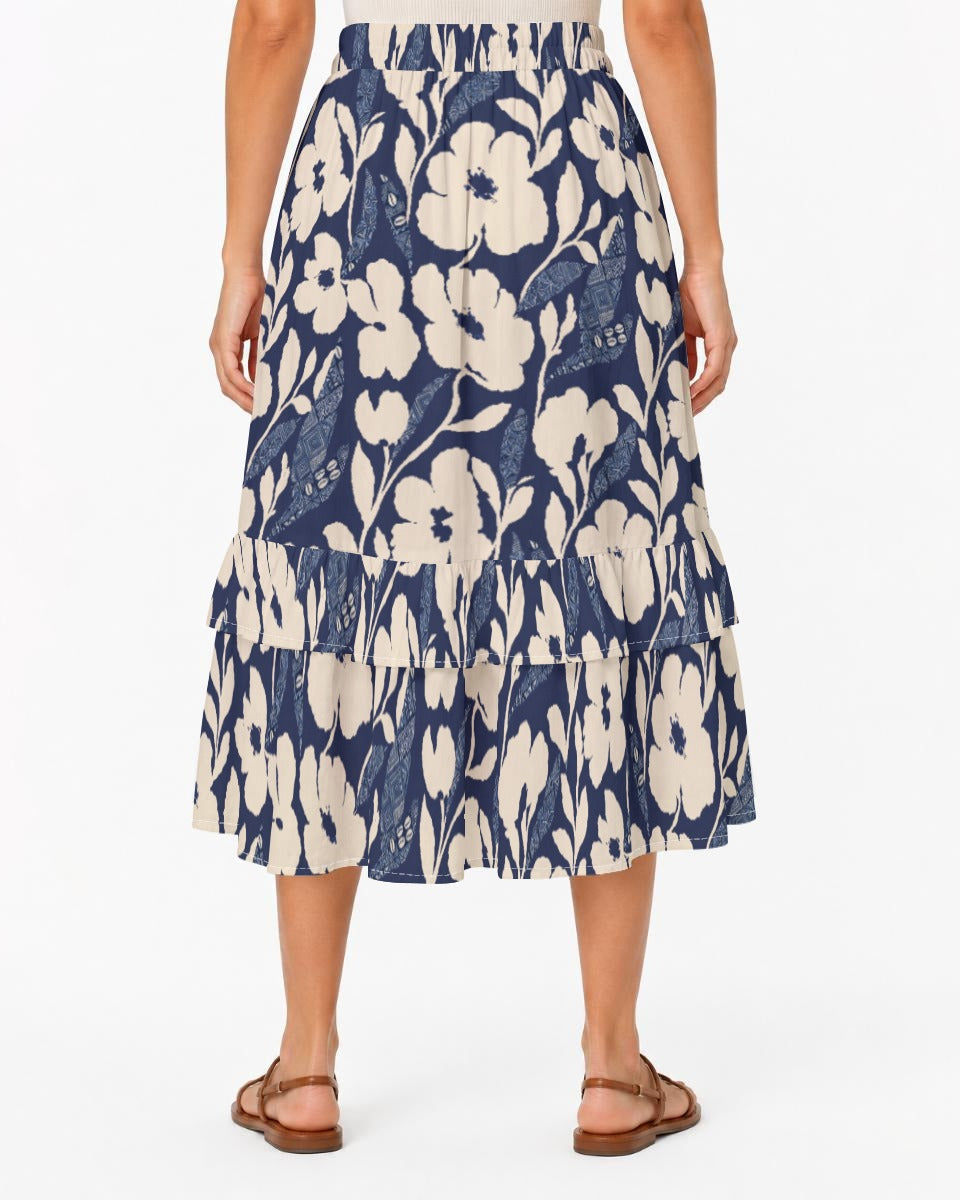 A woman wearing a navy blue and cream floral tiered midi skirt with brown strappy sandals, shown from the back against a plain white studio background.