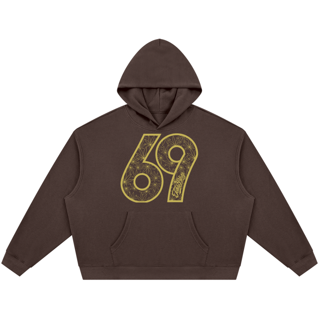 A dark brown cropped hoodie with a large yellow '69' graphic printed on the chest, featuring a detailed mandala pattern inside the numbers.