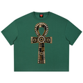 A green short-sleeve crop top t-shirt featuring a large central graphic of an ankh symbol made from plaid and patterned fabrics with circular details.