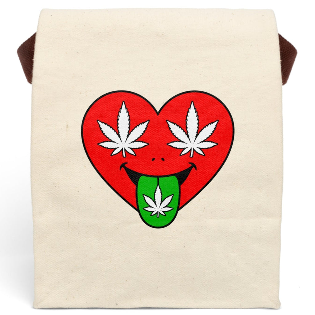 An off-white canvas tote bag with brown shoulder straps, featuring a graphic of a red heart with white cannabis leaves for eyes and a green tongue sticking out with a cannabis leaf.