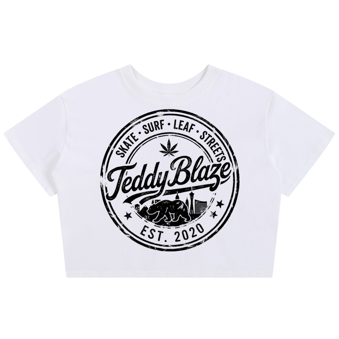 A white cropped short-sleeve t-shirt featuring a large black circular graphic on the front with the text 'Teddy Blaze' and 'EST. 2020' along with 'Skate Surf Leaf Street'.