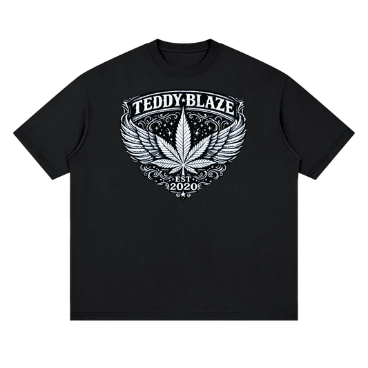 A black short-sleeve crewneck t-shirt with a white graphic print on the chest featuring a winged cannabis leaf, the text 'TEDDY-BLAZE', and 'EST. 2020'.