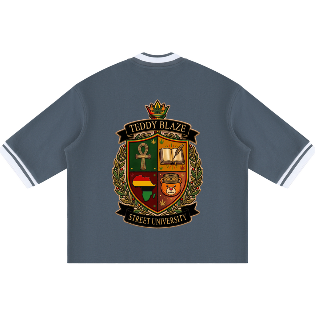 A slate blue short-sleeve t-shirt with white striped collar and cuffs, featuring a large 'Teddy Blaze Street University' crest graphic on the back.