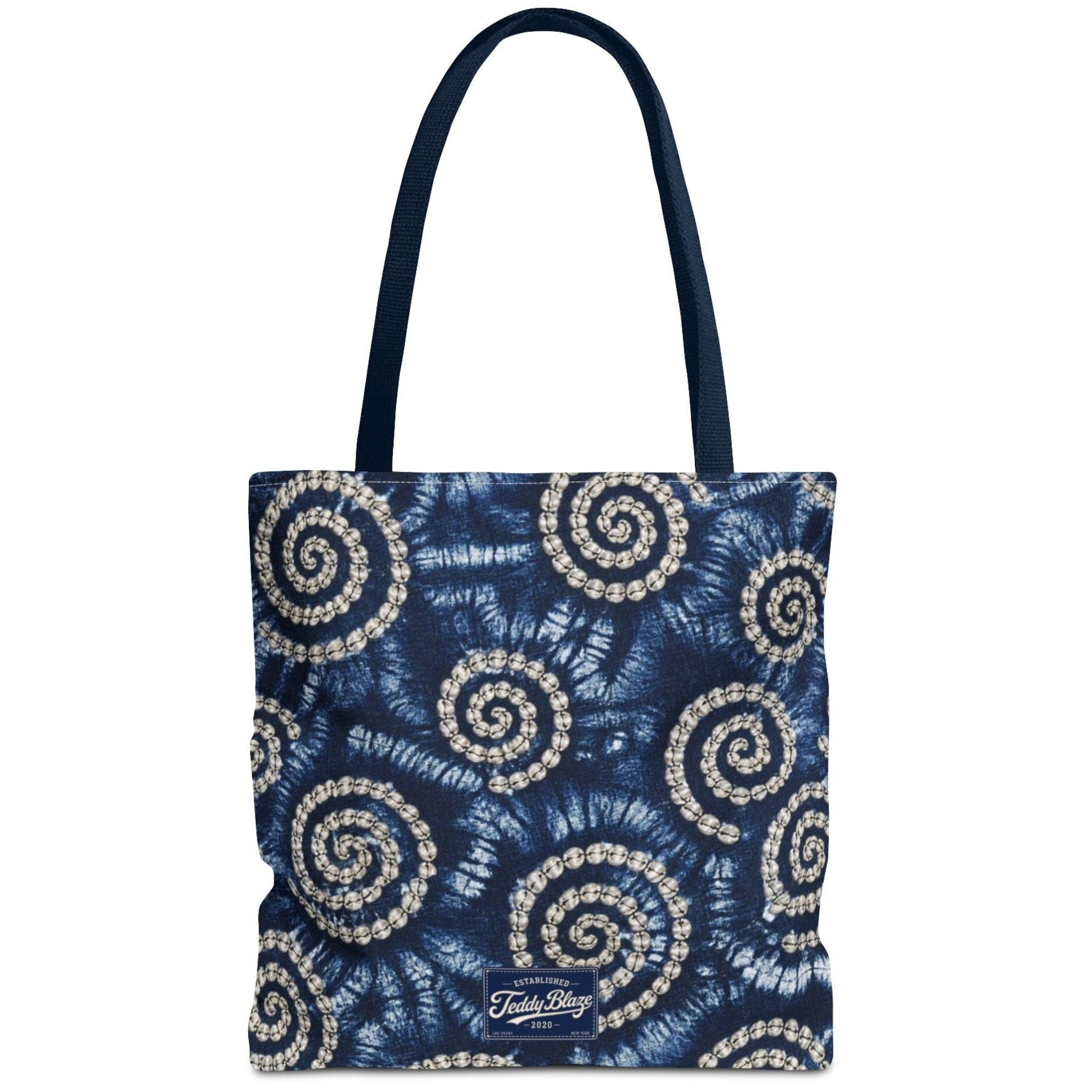 A navy blue tote bag with a white and gray spiral tie-dye pattern, featuring dark navy handles and a small white 'TulaBag' logo patch at the bottom center.