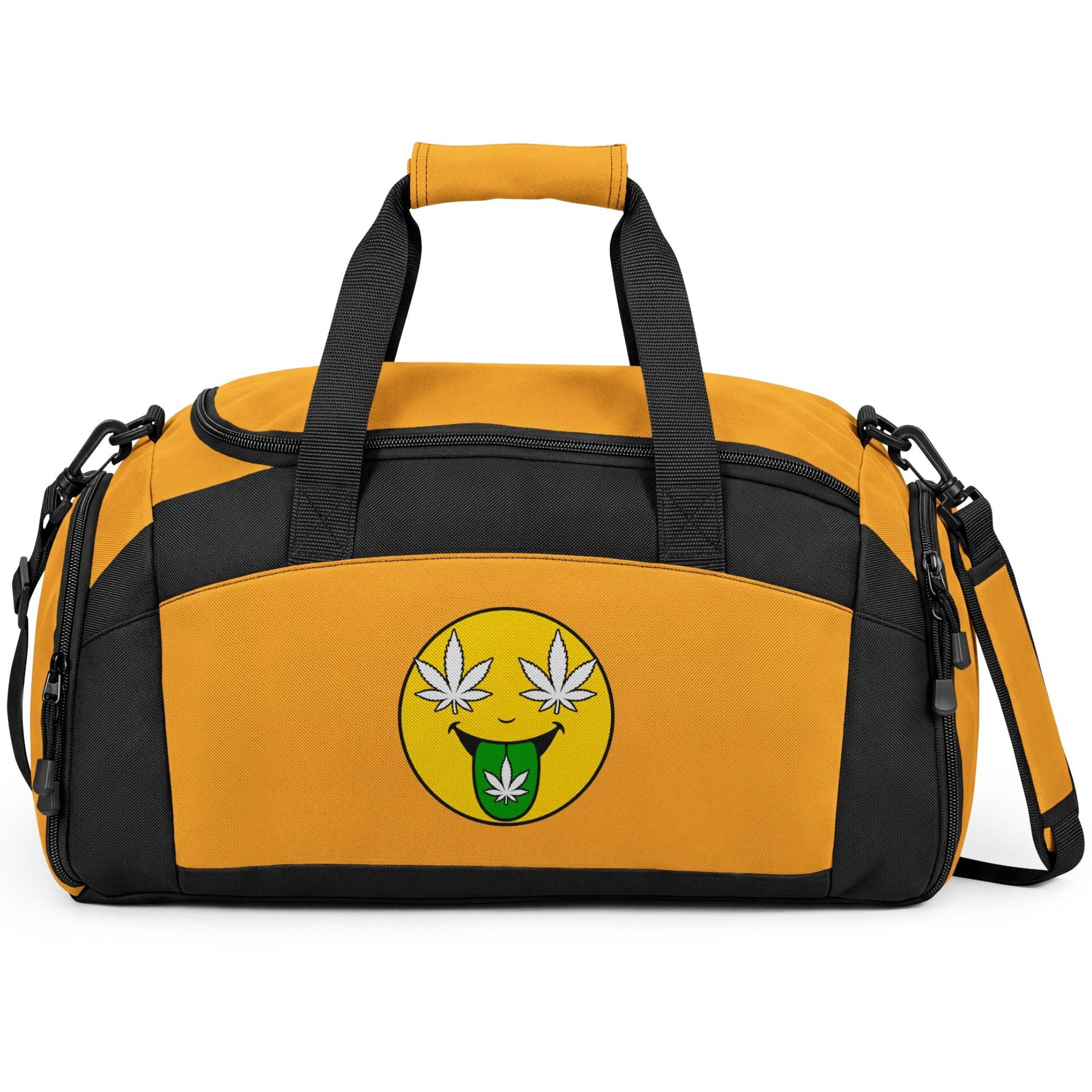 A yellow and black duffel bag with a yellow smiley face graphic on the front featuring white cannabis leaves for eyes and a green leaf on its tongue, shown on a white background.