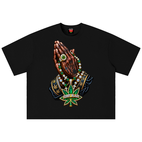 A black short-sleeve t-shirt with a large graphic print of praying hands adorned with a green cannabis leaf ring, green beads, and a green cannabis leaf pendant, displayed on a solid white background.
