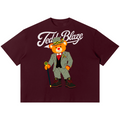 A maroon short-sleeve t-shirt featuring a graphic of a teddy bear in a green checkered suit and hat with the text 'Teddl Blaze' in white script across the chest, displayed on a solid white background.