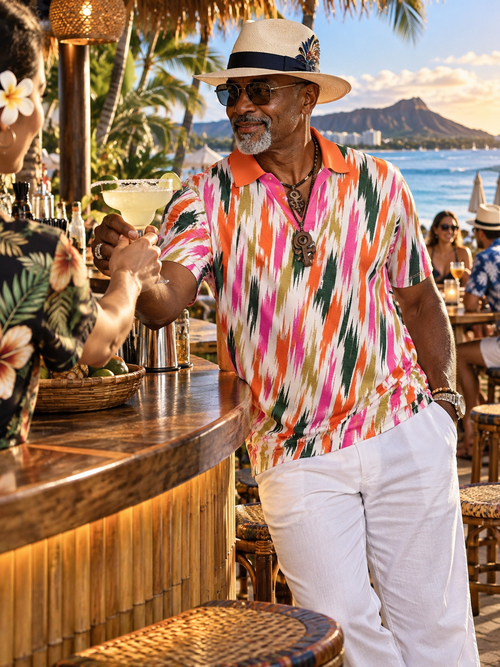 A man wearing a colorful Hawaiian-style short-sleeve polo shirt, white pants, a straw hat, and sunglasses stands at a tropical beach bar, holding a margarita. The background features a scenic view of Diamond Head Crater and the ocean.