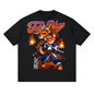 A black short-sleeve crewneck t-shirt featuring a large graphic print of a cartoon bear wearing a blue samurai outfit and holding a sword, with flames on both sides. The text 'Teddy Blaze' is written above in orange and white, with vertical Japanese characters below.