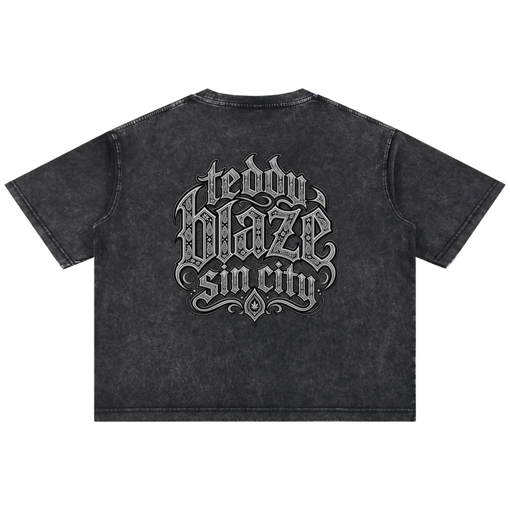 A dark gray acid-wash short-sleeve t-shirt with a large gothic-style graphic on the back reading 'teddy blaze sin city' in white and light gray lettering, shown against a plain white background.