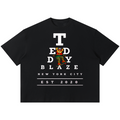 Shop the Boxy Eyechart Tee by Teddy Blaze. 220 GSM cotton-poly oversized drop-shoulder t-shirt with Snellen eye chart graphic from TOPS BY TEDDY BLAZE.