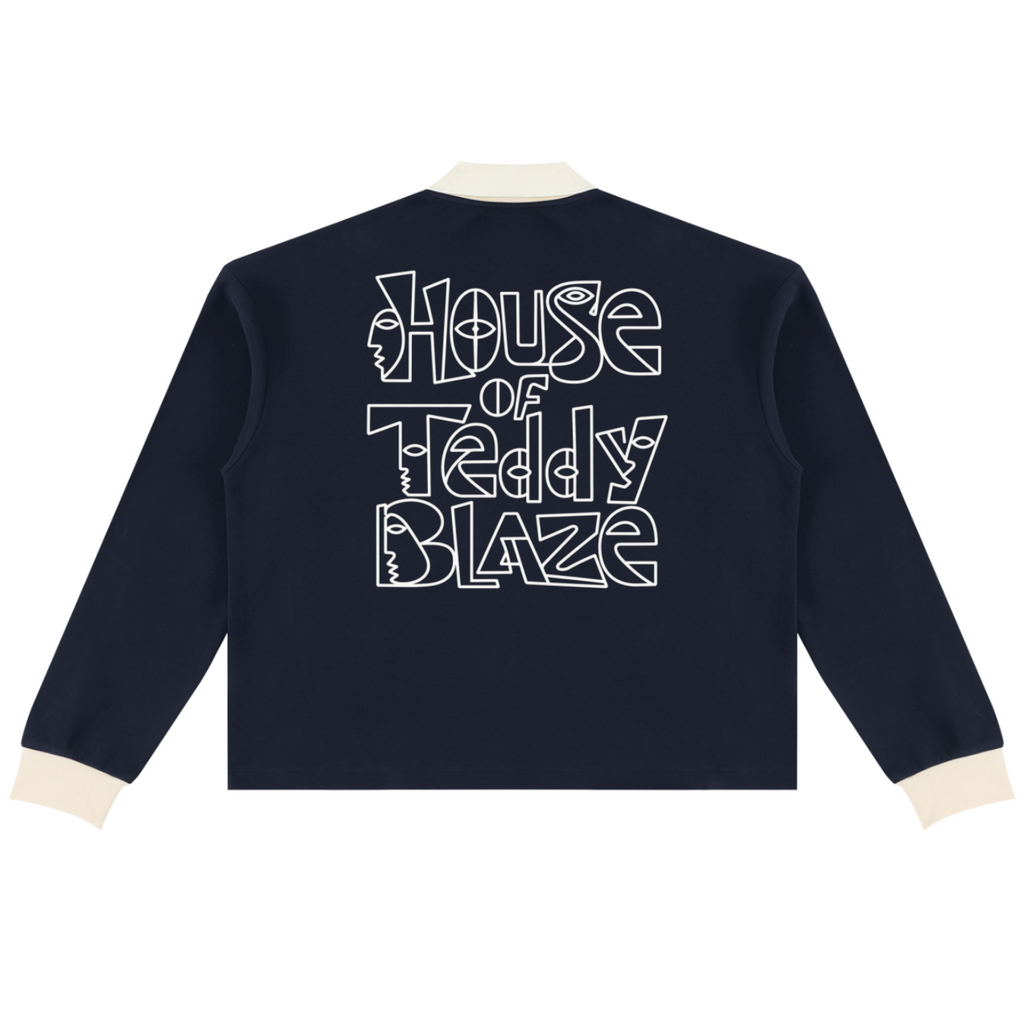 A navy blue long-sleeve cropped jacket shown from the back, featuring a large white graphic text print that reads 'House of Teddy Blaze' with teddy bear silhouettes inside the letters. The jacket has contrasting cream-colored ribbed collar, cuffs, and hem, and is displayed on a clean white background.