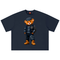 A navy blue short-sleeve t-shirt featuring a graphic of a teddy bear wearing a detailed blue and white patterned outfit with brown boots, displayed flat against a white background.