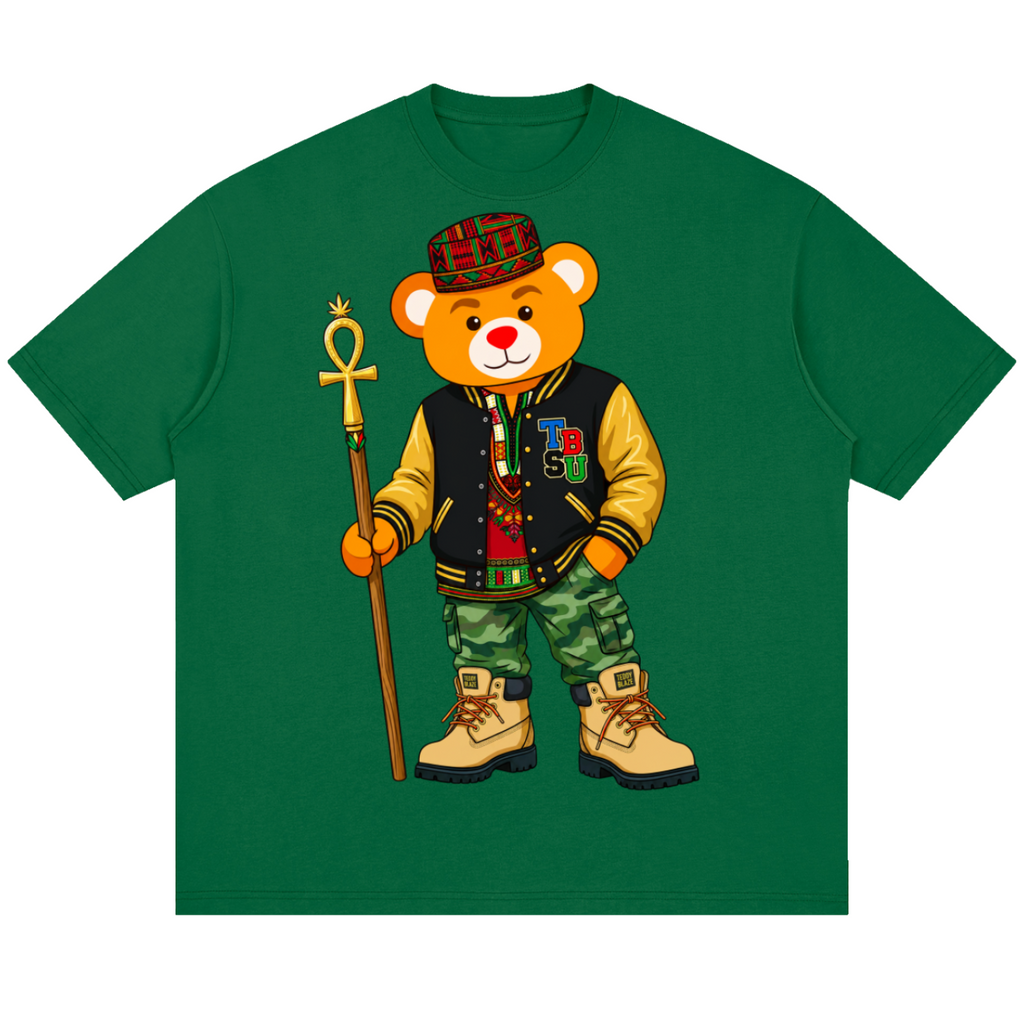 A green short-sleeve crewneck t-shirt featuring a cartoon graphic of a teddy bear dressed in a varsity jacket, camouflage pants, a plaid hat, and holding an ankh symbol staff.