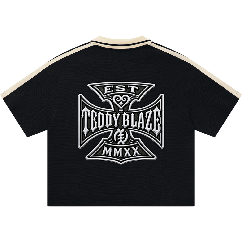 A black short-sleeve t-shirt with cream-colored shoulder stripes and a large white graphic print on the back. The graphic features an ornate shield design with the text 'EST', 'TEDDY BLAZE', and 'MMXX'.