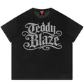 A black short-sleeve t-shirt with a large, ornate silver 'Teddy Blaze' graphic printed across the chest, displayed flat against a solid white background.