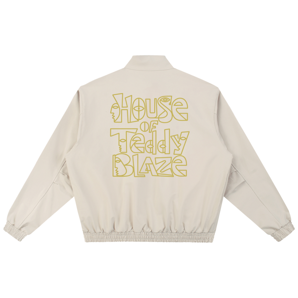 A beige jacket shown from the back, featuring the text 'House of Teddy Blaze' printed in a yellow outline font across the upper back.