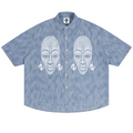 A short-sleeve button-up shirt in a heathered light blue fabric, featuring a white graphic print of two stylized African masks with ear ornaments across the chest.