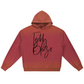 A cropped pullover hoodie with a warm red-orange gradient, featuring the words 'Teddy Blaze' printed in a black cursive script across the chest, displayed on a solid white background.