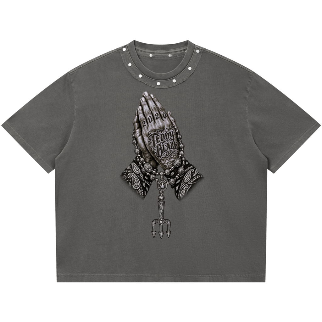 Elevate your boxy graphic tees with the Teddy Blaze Sin City Sacred Snow Wash Studded Cotton Tee. Charcoal snow-washed cotton, metal studded collar, and tattoo praying hands print. Shop NYC to Vegas style.