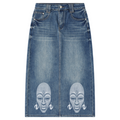 A medium wash blue denim skirt with two large white printed African face masks on the lower front, displayed flat against a white background.